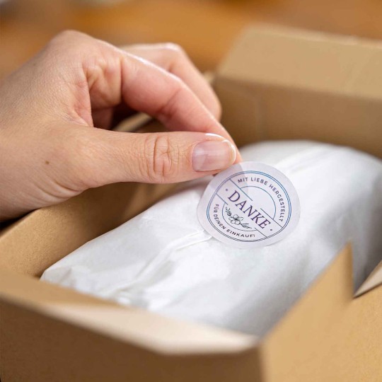 Rund etiket bliver sat på et silkepapir i en papkasse som del af branding.