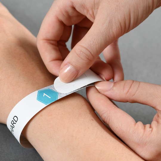 Selvklæbende entréarmbånd bliver fastgjort om et håndled.
