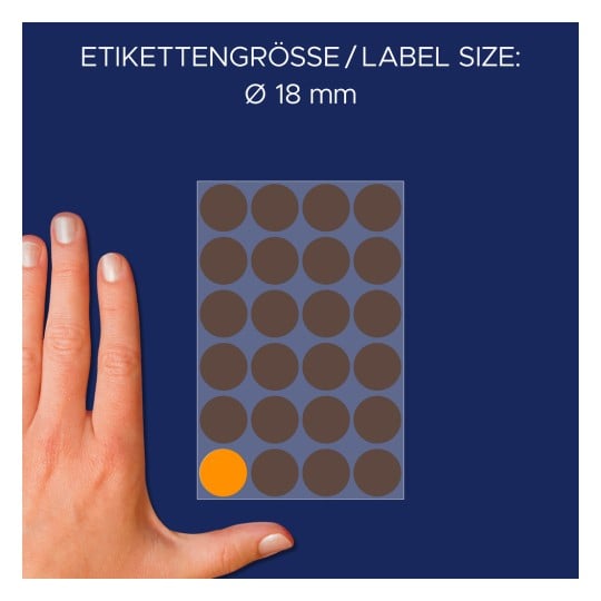 Billedet viser en hånd ved siden af et ark med cirkulære etiketter, der angiver størrelsen 18 mm med forskellige brune cirkler og én orange cirkel i nederste venstre hjørne.