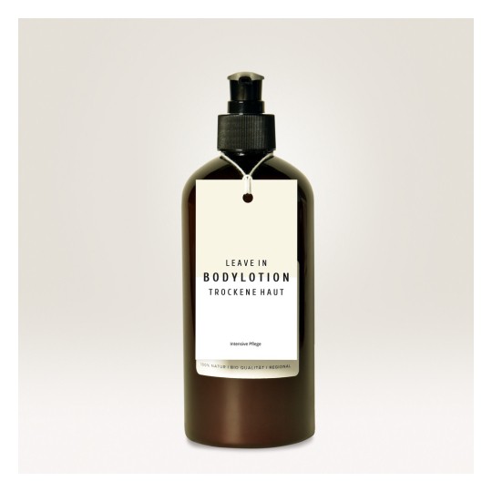 Billedet viser en mørkebrun flaske med bodylotion med en etiket, der læser 'LEAVE IN BODYLOTION TROCKENE HAUT' og 'Intensive Pflege'. Flasken har en pumpe-top og et minimalistisk design.