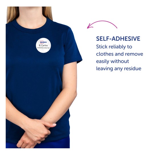 Billedet viser en person iført en marineblå t-shirt med et selvklæbende navneskilt, der siger 'B. Carlos MARKETING DIREKTØR'. Teksten til højre fremhæver det selvklæbende træk, og understreger dens pålidelighed samt at den kan fjernes uden at efterlade rester.