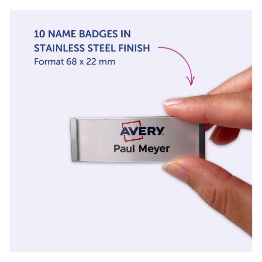 Billedet viser en hånd, der holder et navneskilt i rustfrit stål finish med teksten 'Avery' og navnet 'Paul Meyer'. Det fremhæver, at der er 10 navneskilte tilgængelige i det specificerede format på 68 x 22 mm.