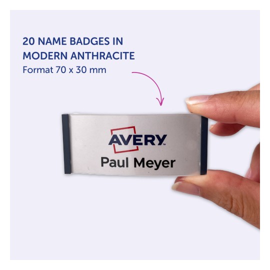 Billedet viser en hånd, der holder et navneskilt mærket 'Avery' med navnet 'Paul Meyer', hvilket indikerer, at det er en del af et sæt på 20 skilte i moderne antracitfarve, der måler 70 x 30 mm.