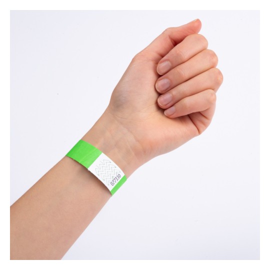 Et nærbillede af en hånd med et grønt armbånd på håndleddet. Armbåndet har en hvid sektion med et zigzag-design og ser ud til at være mærket med et nummer.