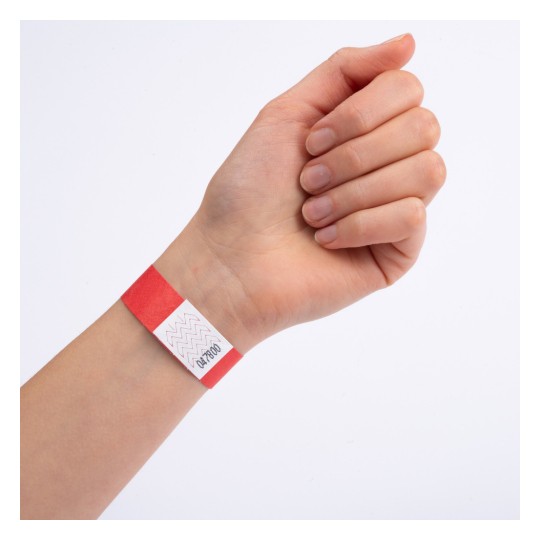 En hånd med et rødt armbånd med en hvid etiket, der har zigzag-mønstre og tal trykt på.