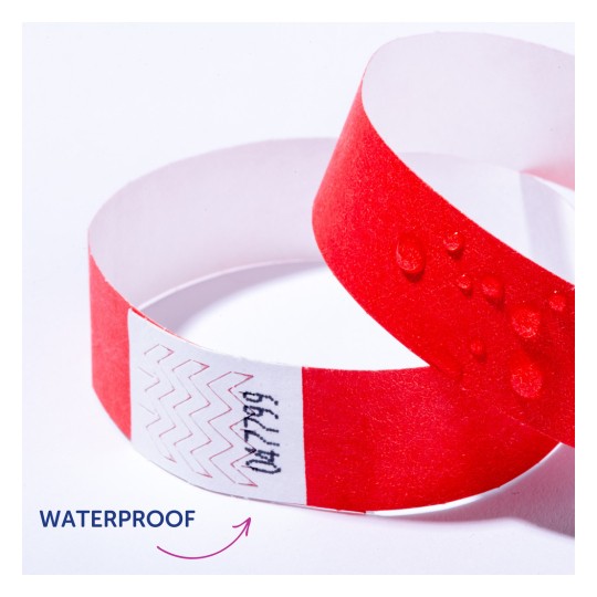 Billedet viser et rødt vandtæt armbånd med vanddråber på det. Der er zigzag mønstre og tekst på en hvid stribe af armbåndet.