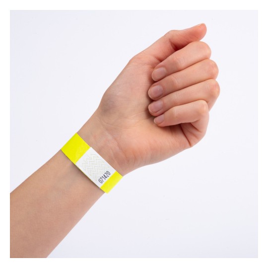 Dette billede viser en hånd med et gult armbånd, som har et hvidt afsnit med et zigzag-mønster og et nummer på det.