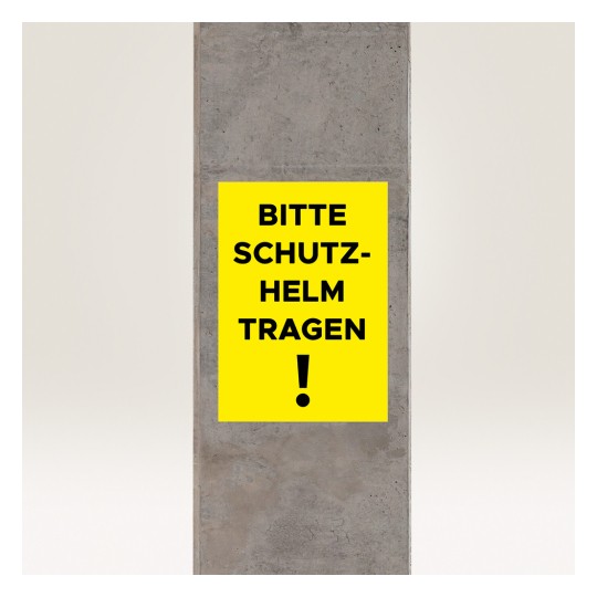 Billedet viser et gult skilt på en betonpille, hvor der står 'BITTE SCHUTZ-HELM TRAGEN!', hvilket oversættes til 'Venligst brug hjelm!' og angiver et sikkerhedskrav.