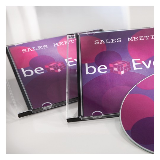 Billedet viser to CD-etuier med titlen 'Sales Meeting' og en disc med et farverigt design. Designet indeholder cirkler i nuancer af pink og lilla, sammen med teksten 'beEven.'