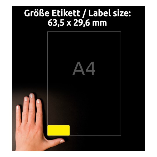 Billedet viser en hånd placeret nær en etiketstørrelsestabel, der viser dimensioner på 63,5 x 29,6 mm med en 'A4' betegnelse. Baggrunden er mørk, hvilket forbedrer synligheden af etiketten og teksten.