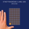 Billedet viser en hånd ved siden af et ark med etiketter, der angiver en etiketterstørrelse på 12 mm i diameter med mørkebrune cirkler og én orange cirkel.