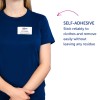 Billedet viser en person iført en marineblå skjorte med et navneskilt, der lyder 'B. Carlos, Marketing Director.' Derudover er der tekst, der beskriver navneskiltets selvklæbende egenskab, som siger, at det hæfter pålideligt på tøj og let fjernes uden at efterlade nogen rester.