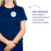 Billedet viser en person iført en marineblå t-shirt med et selvklæbende navneskilt, der siger 'B. Carlos MARKETING DIREKTØR'. Teksten til højre fremhæver det selvklæbende træk, og understreger dens pålidelighed samt at den kan fjernes uden at efterlade rester.