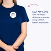 Billedet viser en person iført en blå t-shirt med et selvklæbende navneskilt, der lyder 'B. Carlos, Marketing Director.' Teksten fremhæver, at skiltet sidder godt fast på tøjet og kan fjernes nemt uden at efterlade rester.