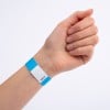 Billedet viser en hånd iført et blå- og hvidstribet armbånd. Armbåndet har en kode trykt på det, som muligvis angiver adgang eller entré til en begivenhed.