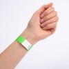 Et nærbillede af en hånd med et grønt armbånd på håndleddet. Armbåndet har en hvid sektion med et zigzag-design og ser ud til at være mærket med et nummer.