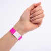 Billedet viser en hånd med et pink armbånd, der har en hvid etiket og et nummer trykt på. Hånden er placeret med fingrene lukkede, og armbåndet er tydeligt synligt.