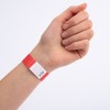 En hånd med et rødt armbånd med en hvid etiket, der har zigzag-mønstre og tal trykt på.