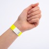 Dette billede viser en hånd med et gult armbånd, som har et hvidt afsnit med et zigzag-mønster og et nummer på det.