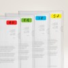 Billedet viser en række gennemsigtige plastikmapper placeret side om side, hver mærket for at indikere sektioner organiseret efter bogstavintervaller: A-D i rød, E-H i grøn, I-R i blå, og S-Z i gul. De indeholder trykte dokumenter, selvom teksten delvist er skjult.