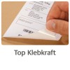 Billedet viser en hånd, der fjerner en etiket fra en papkasse, hvor en leveringsadresse er synlig sammen med en stregkode. Teksten 'Top Klebkraft' vises under billedet, hvilket antyder stærk klæbeevne.